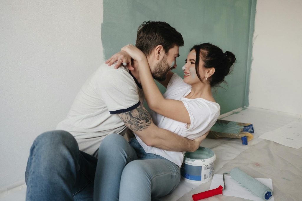 Laughing couple embraces while painting walls during a home renovation.