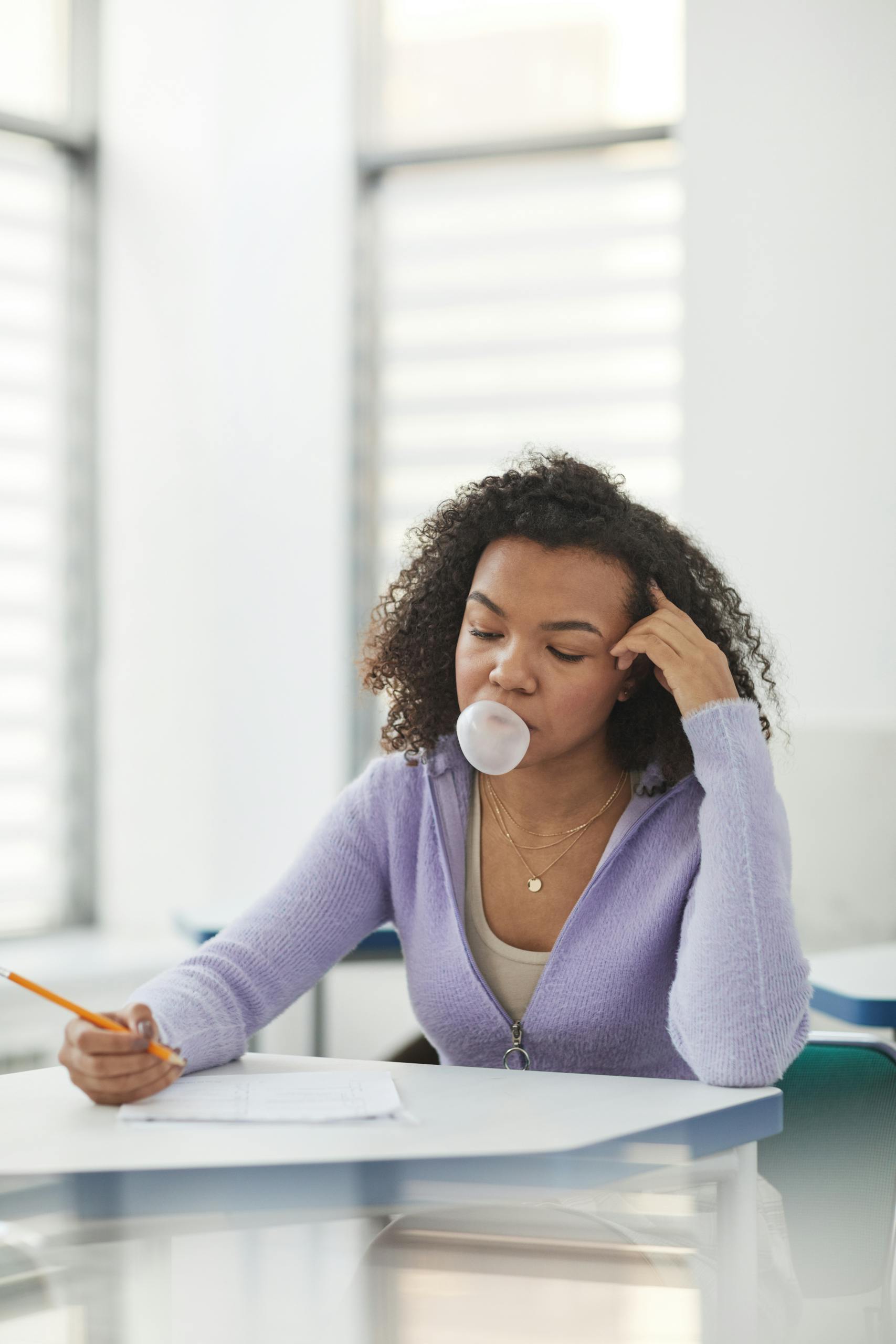 A focused student in a classroom blowing bubble gum while studying for exams.
