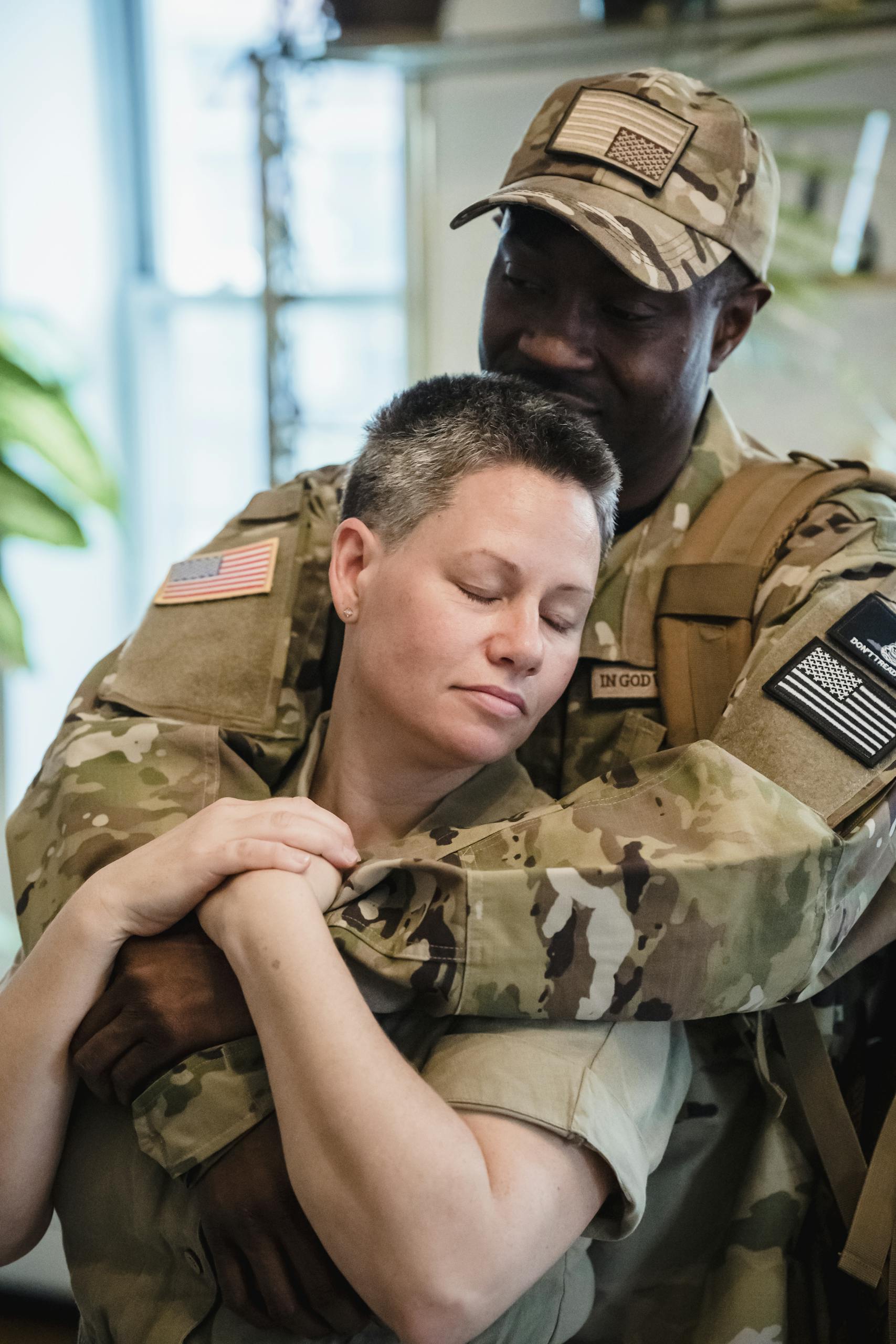 A multiracial military couple sharing an affectionate embrace indoors, showcasing love and unity.