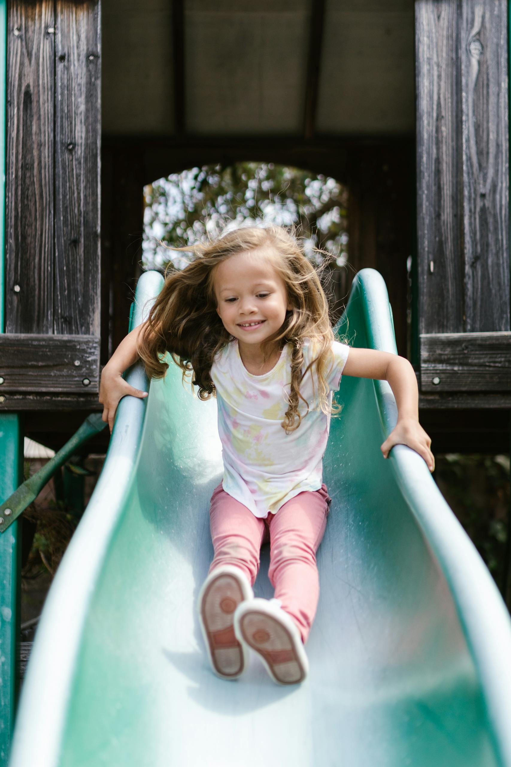 A cheerful girl sliding down a playground slide outdoors during the day trying to address ADHD symptoms.