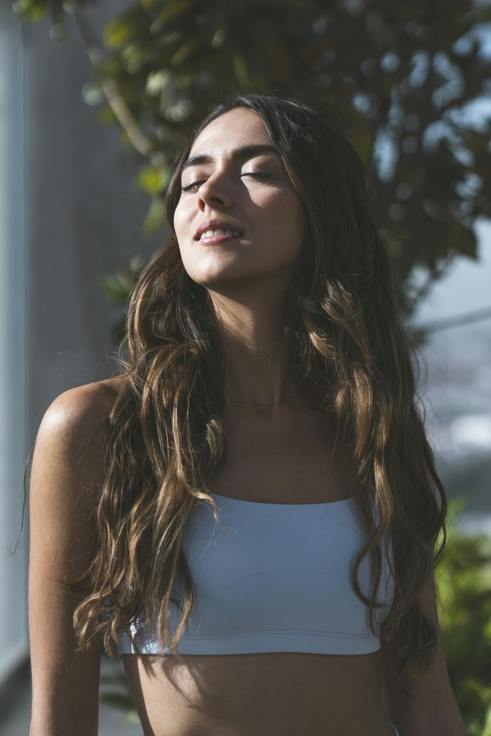 A serene woman with long hair basks in sunlight, meditating in nature, embodying mindfulness and tranquility.