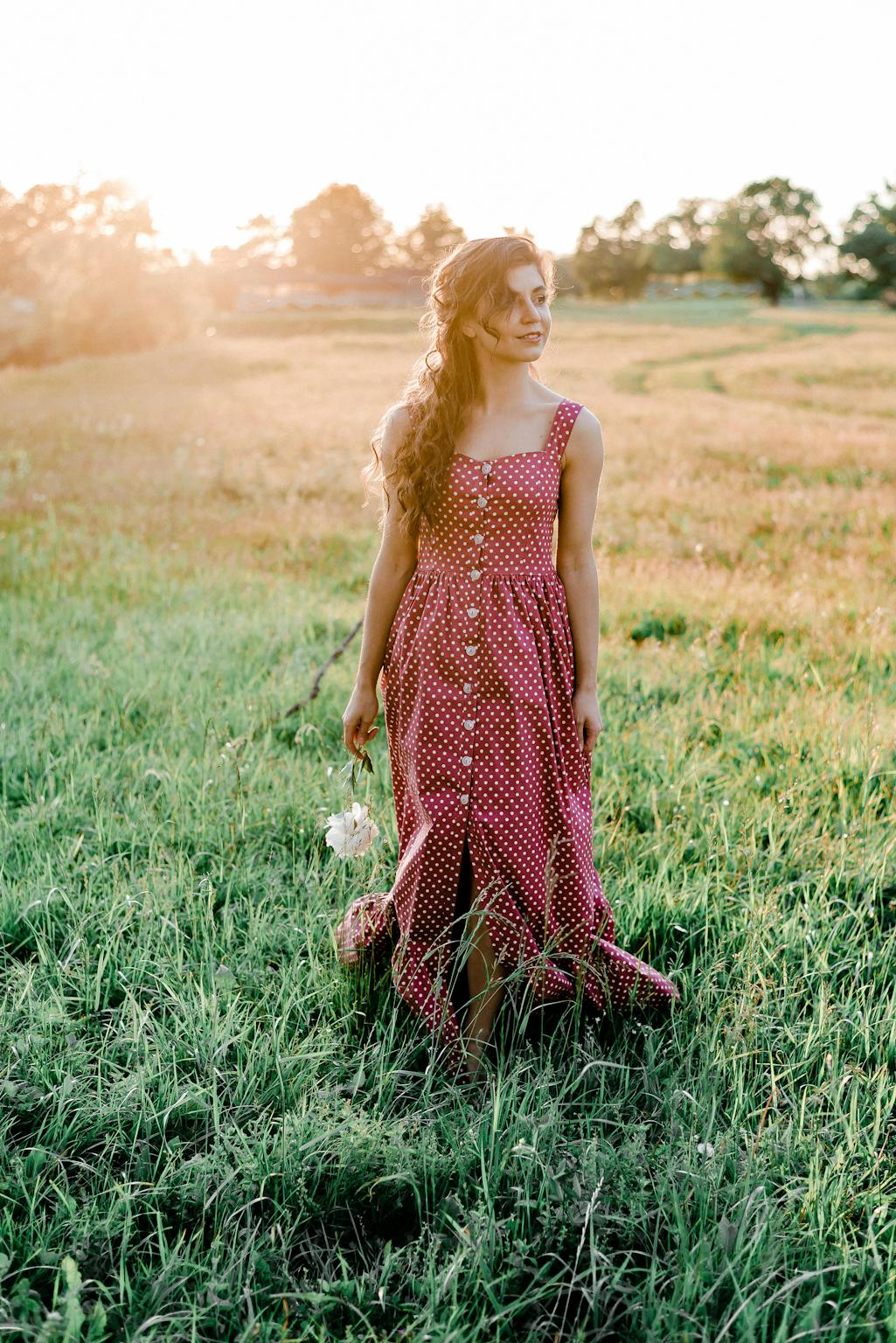 A woman in a red polka dot dress strolls through a sunlit field, embodying summer freedom and reflection