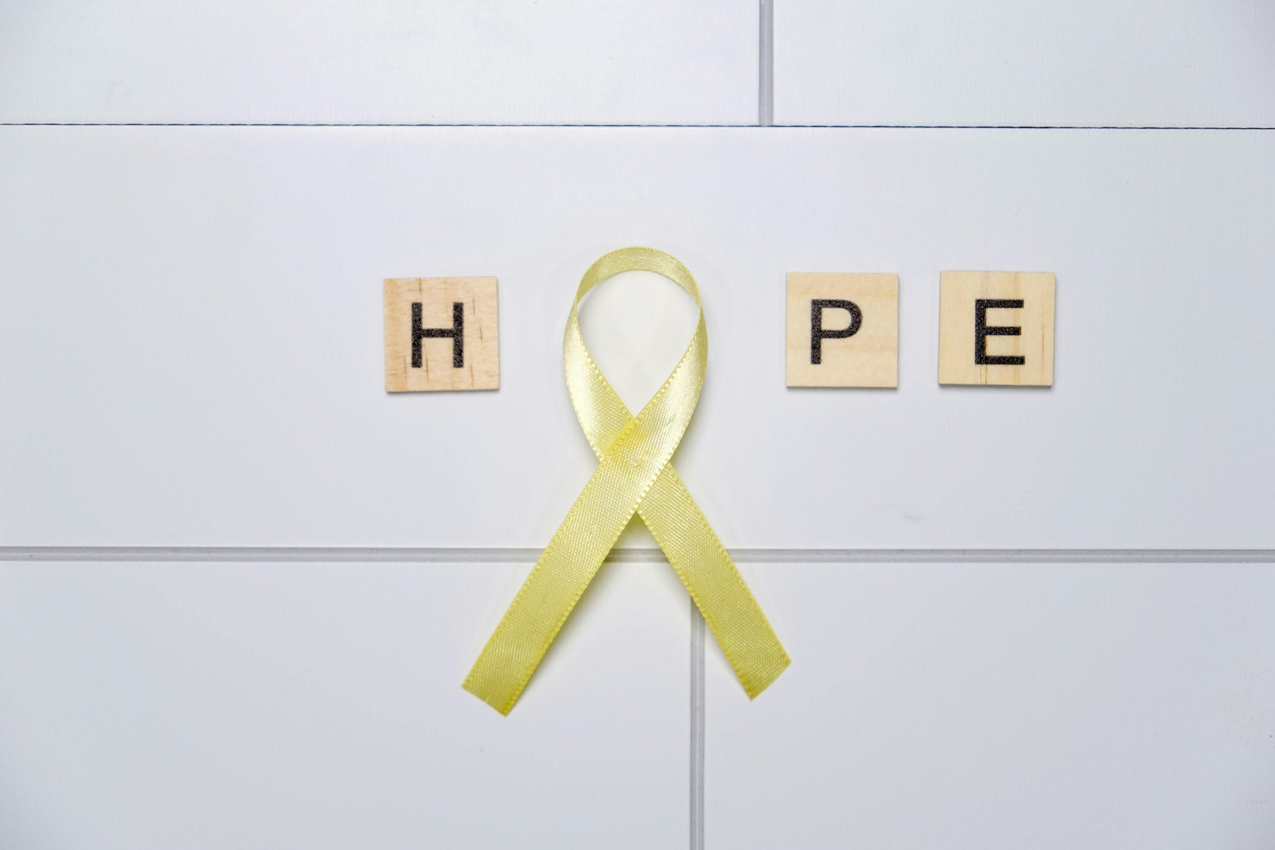 Yellow awareness ribbon forming 'O' with HOPE on tiles, symbolizing support and positivity.